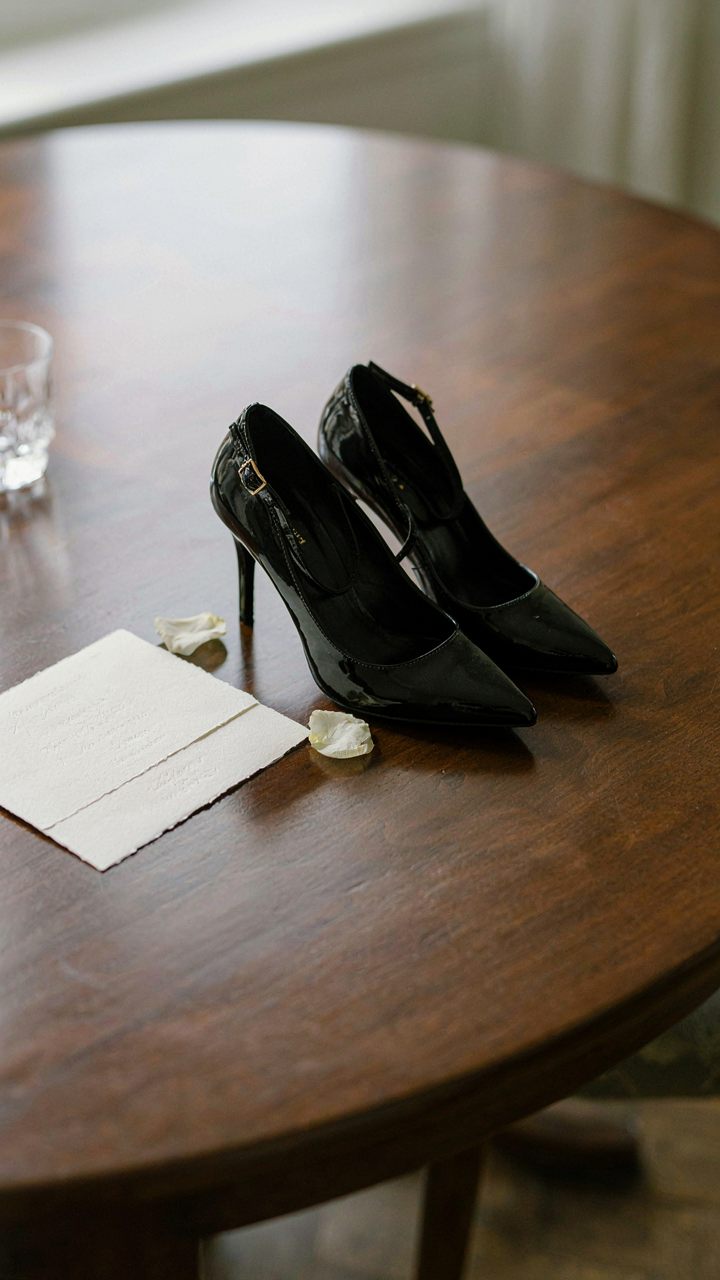 Black stiletto heels are next to a formal black-tie wedding invitation.