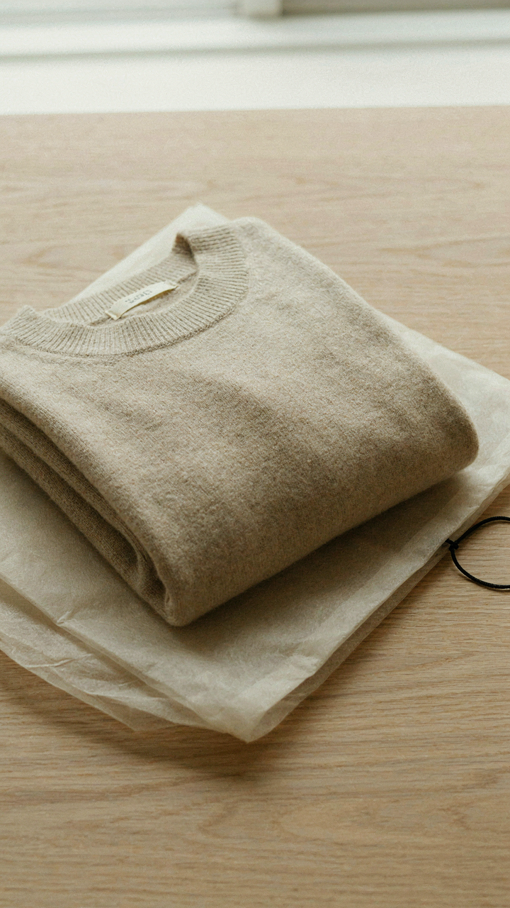 A soft cashmere sweater sits neatly folded in a dry cleaning bag.