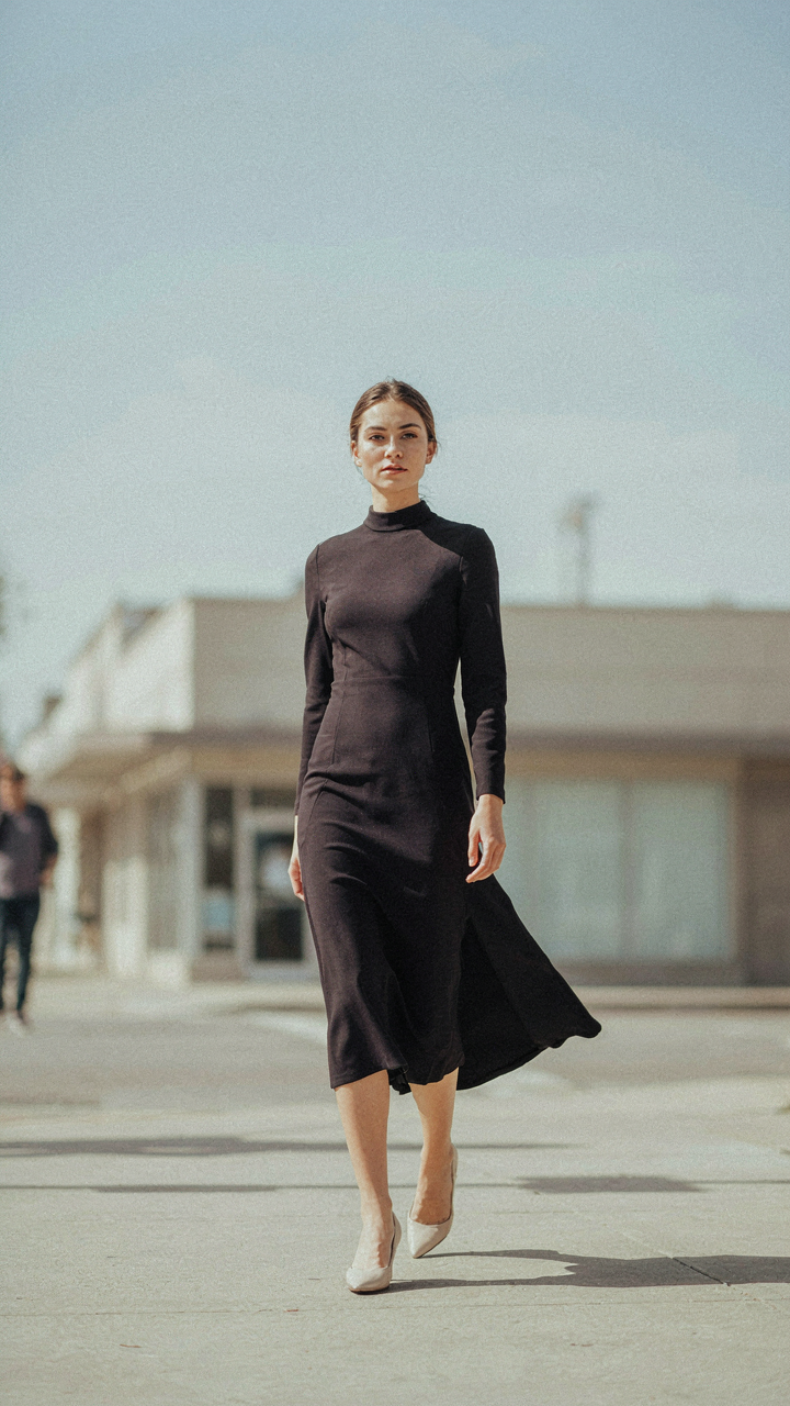 A woman in a dark high neck high-low midi dress walking with fluid movement.