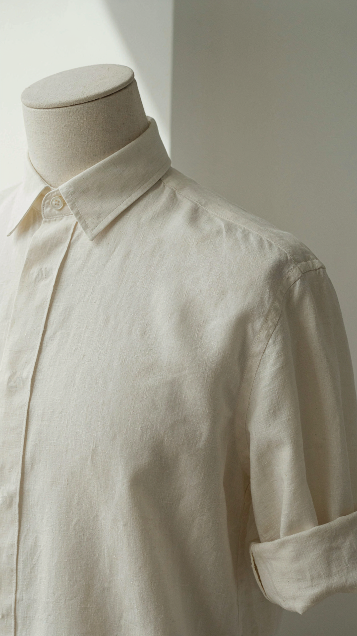 Close-up of a well-fitted cream linen shirt on a mannequin, showing light fabric.