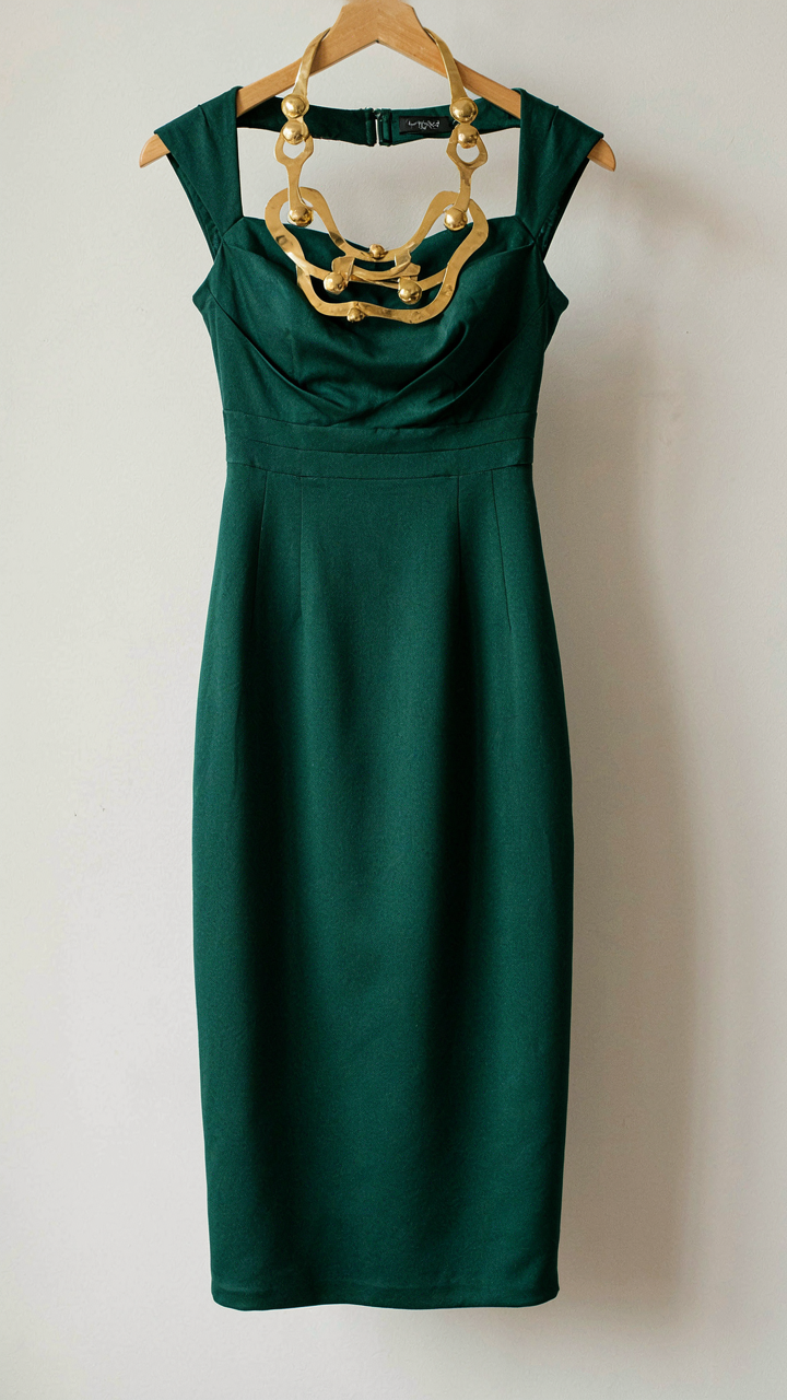 A sculptural brass necklace rests on a solid color cocktail dress.