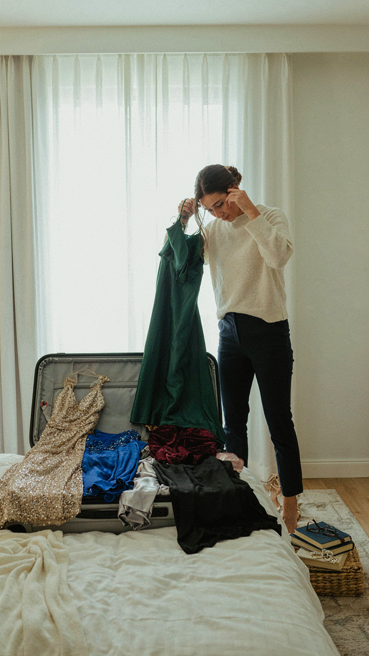 Woman looking stressed at an overflowing suitcase of formal dresses.
