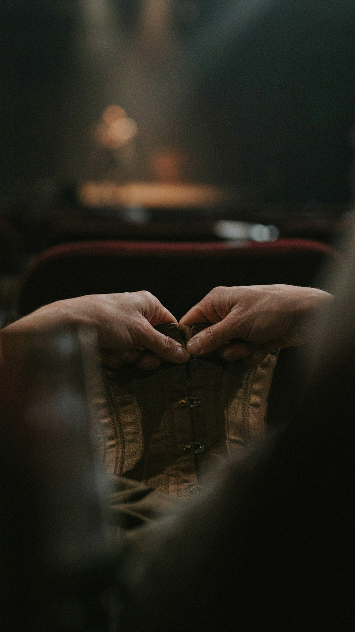 Hands adjusting a tight waistband while sitting in a dark theater seat.