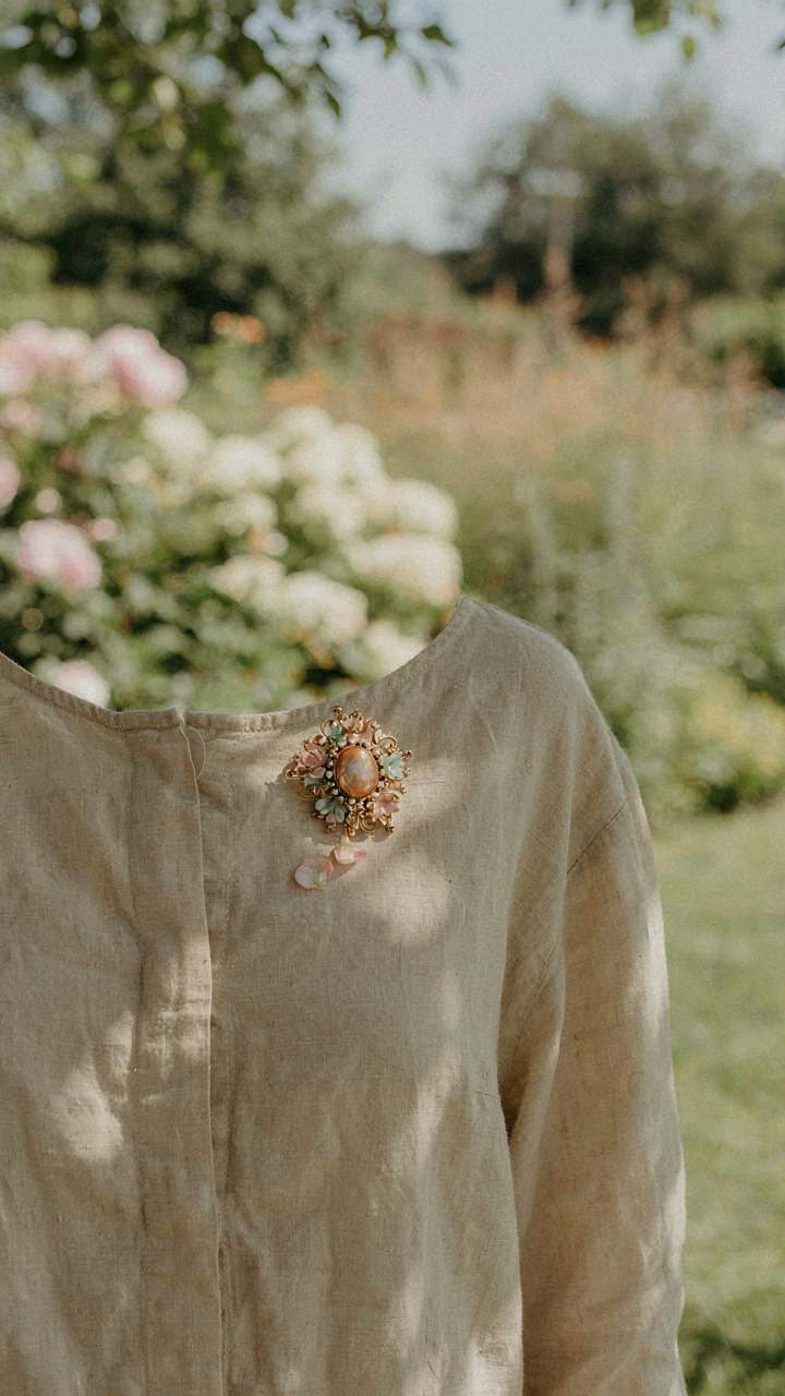 A vintage brooch is pinned to a simple linen dress, catching the light.