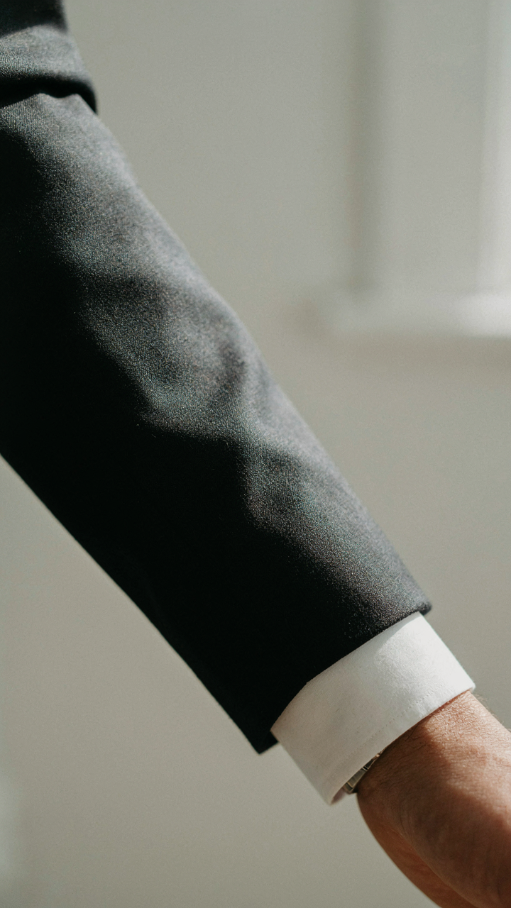 A close-up shows a perfectly fitted blazer sleeve on a person's wrist.
