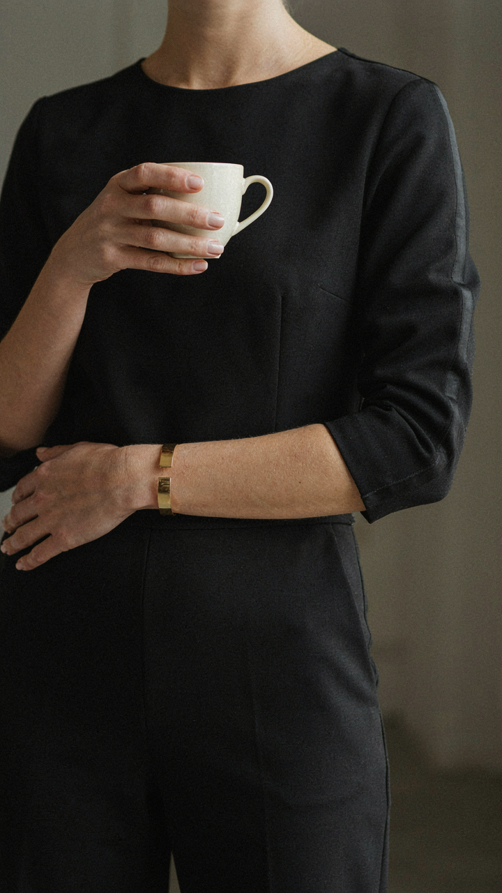 A gold metal cuff bracelet adds impact to a dark wedding guest jumpsuit.