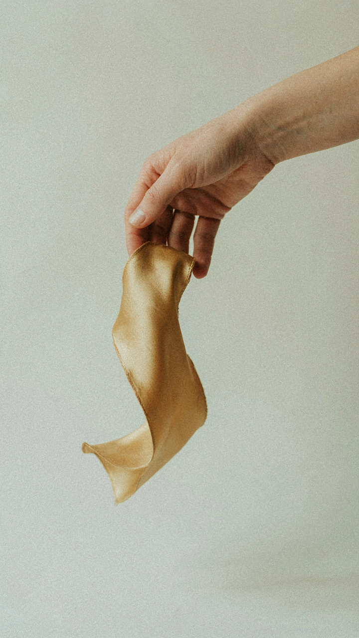 A hand gently drops a shimmering gold silk fabric, showing its light weight.