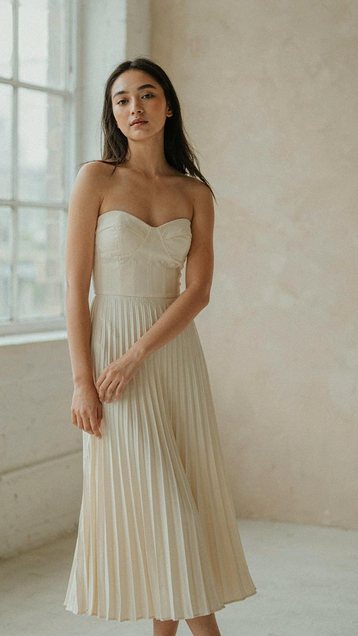 Woman in a pleated midi dress with sweetheart neckline and fitted bodice.