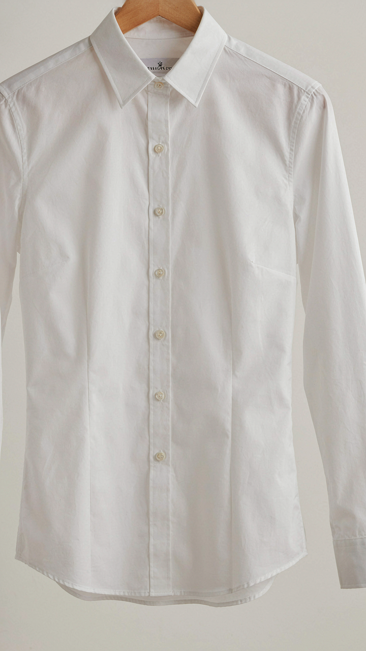 A perfectly tailored white button-down shirt hangs on a wooden hanger.