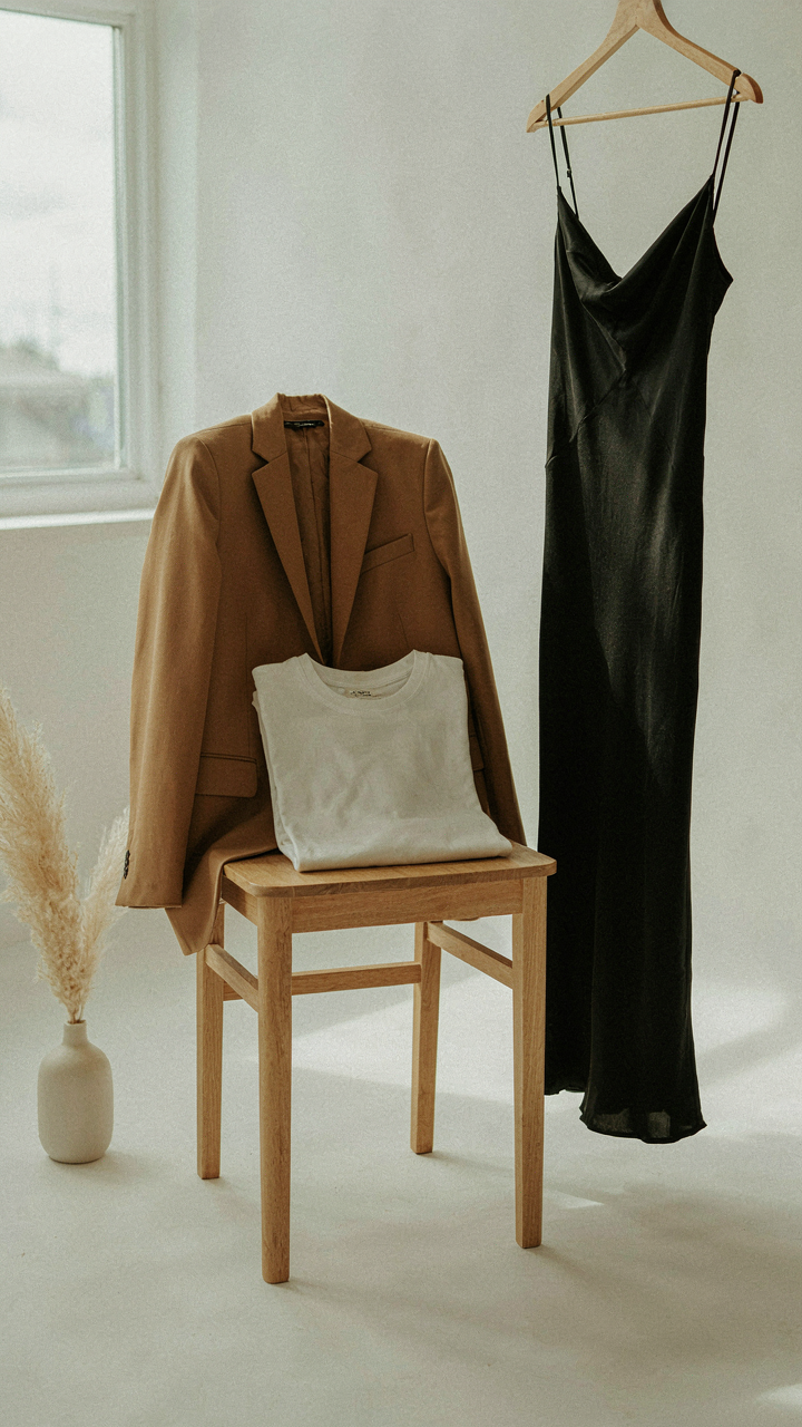 A neutral blazer draped over a chair near a t-shirt and dress, creating multiple looks.