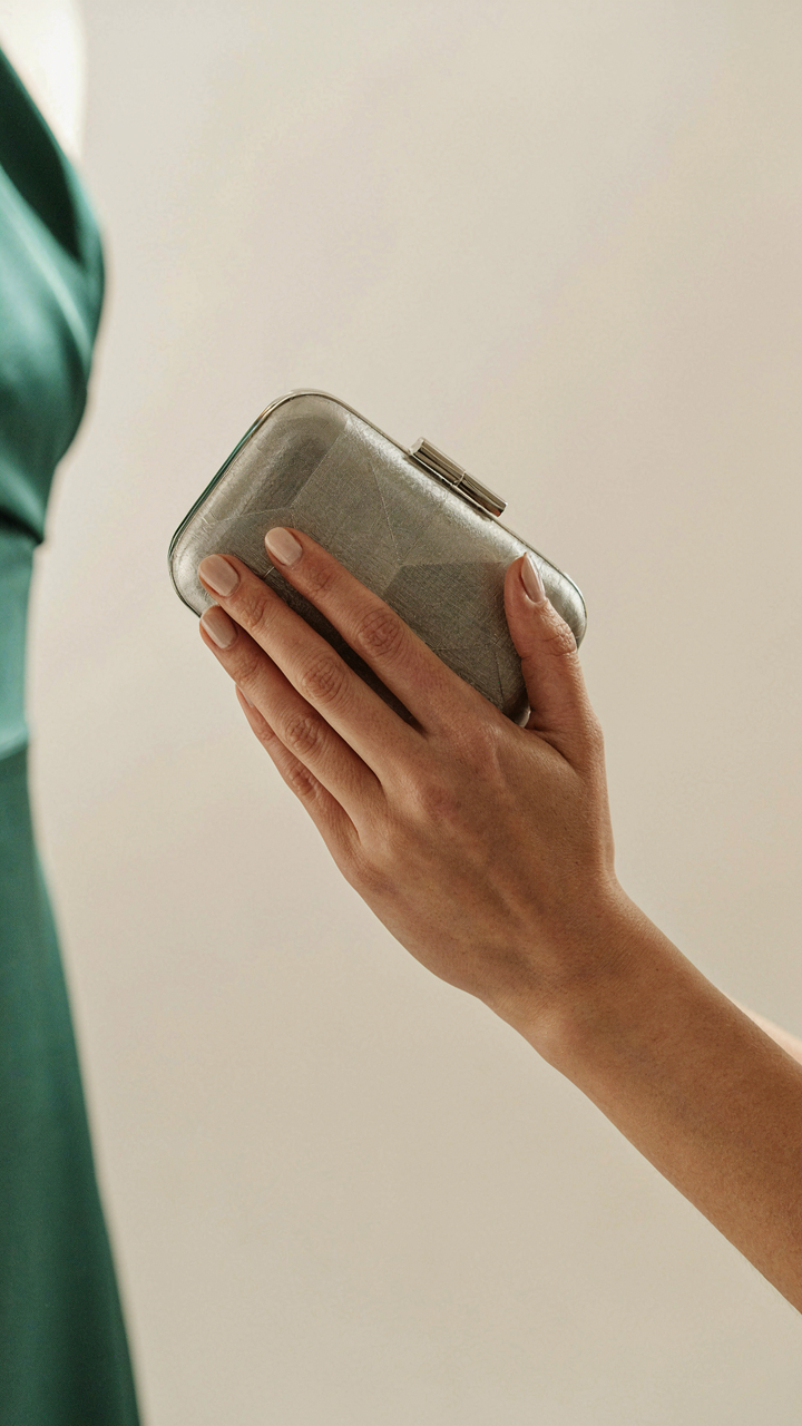 A woman holds a metallic clutch with geometric patterns.