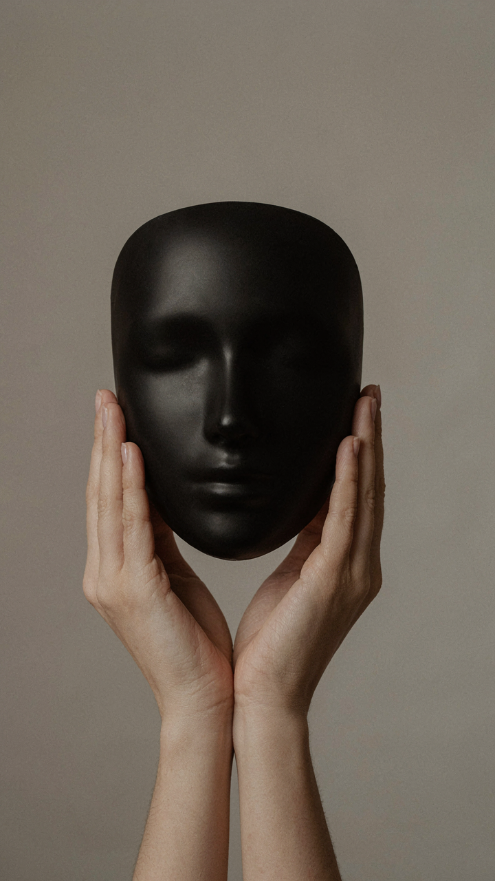 Hands holding a minimalist black mask that matches skin tone.