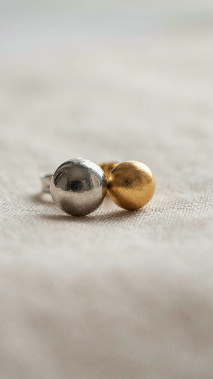 Close-up of polished silver and brushed gold earrings reflecting light.