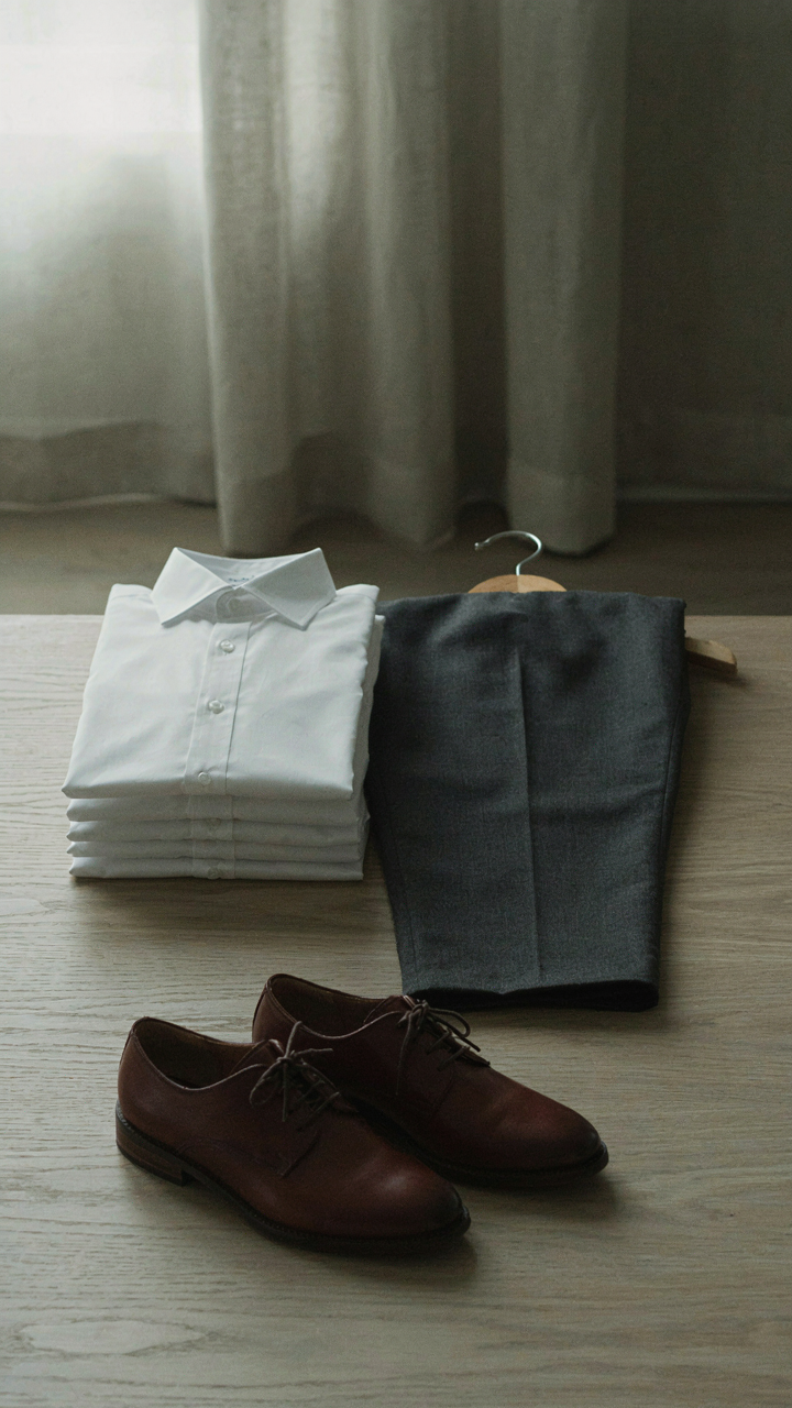 A neatly folded collared shirt, creased trousers, and closed-toe shoes hang together.