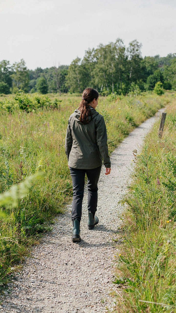A person in flat, rubber-soled boots walks uphill on a gravel path.