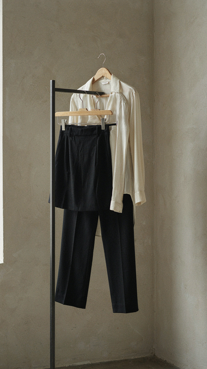 A silk blouse is perfectly tucked into structured black trousers on a clothing rack.