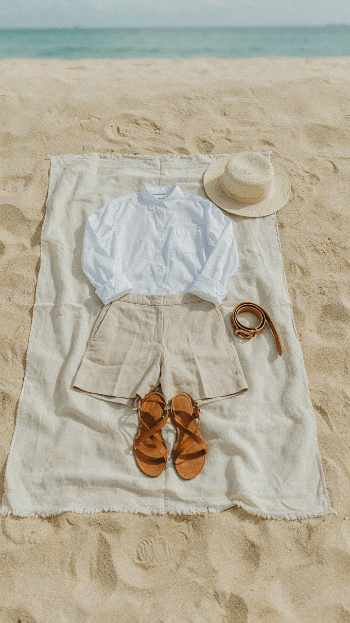 A structured shirt, tailored shorts, and belt laid out on a beach blanket.