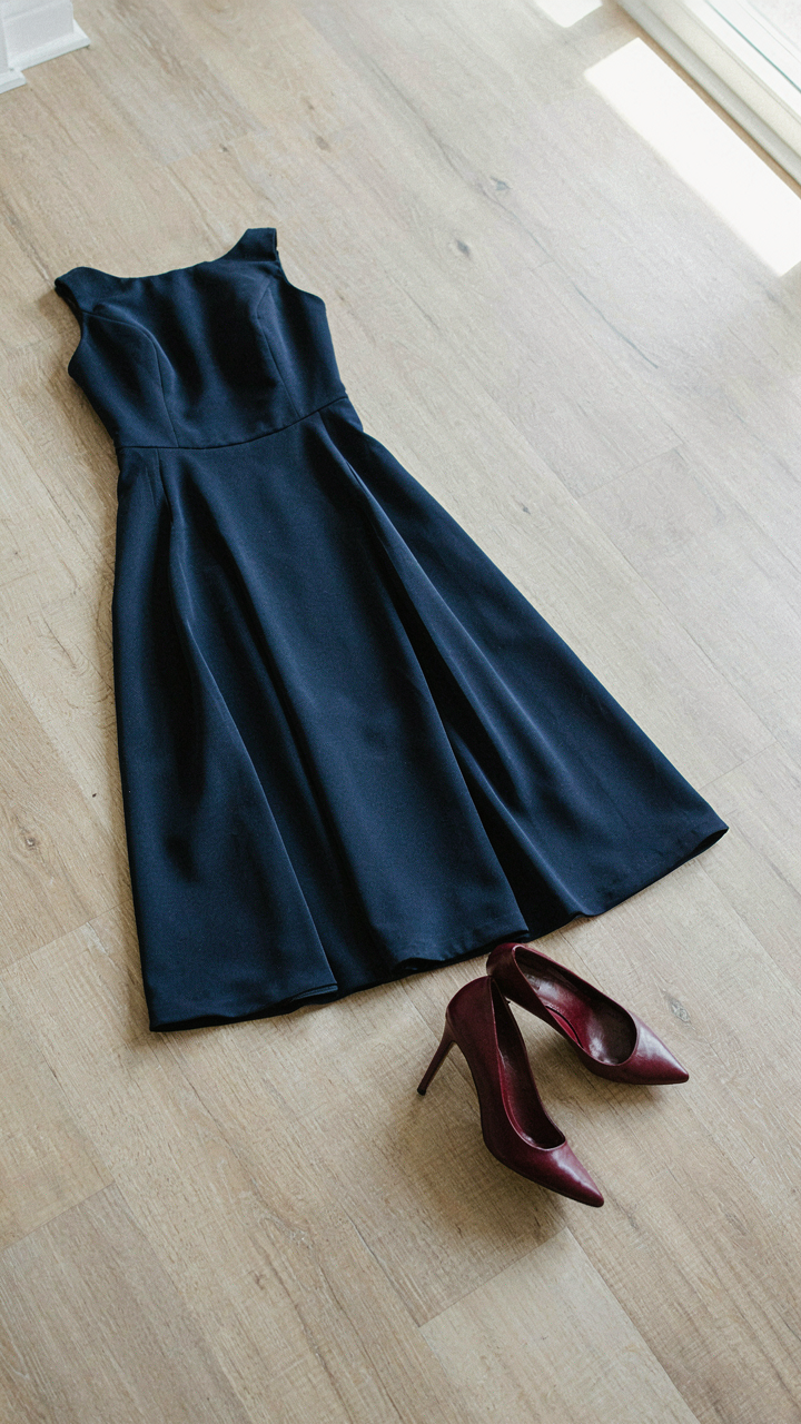 A navy blue cocktail dress next to deep burgundy leather pumps.