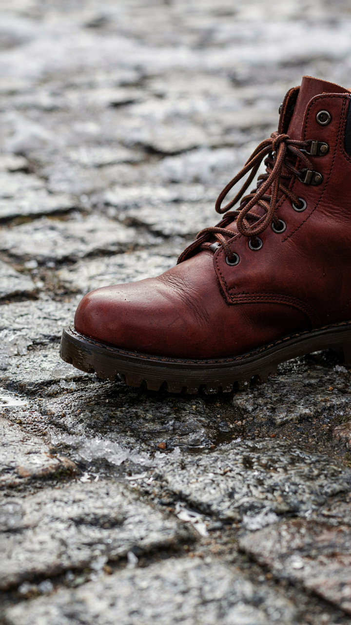 A sturdy, oil-treated leather winter boot stands on a wet, slushy street.