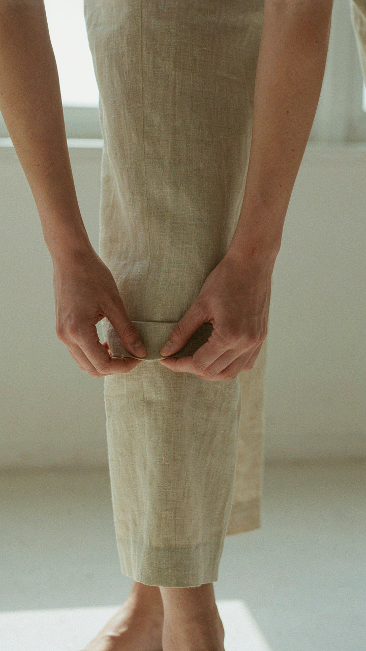 A hand adjusts the hem of a tailored lightweight trouser for a precise fit.