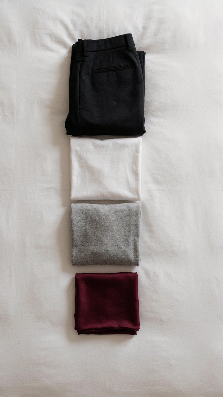A small collection of neutral and accent clothing items laid out on a bed.