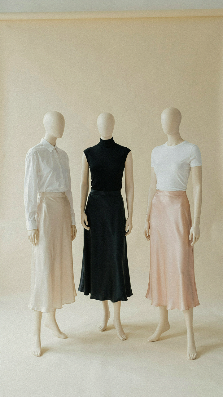 Three mannequins, each in a satin midi skirt, with different fitted tops.
