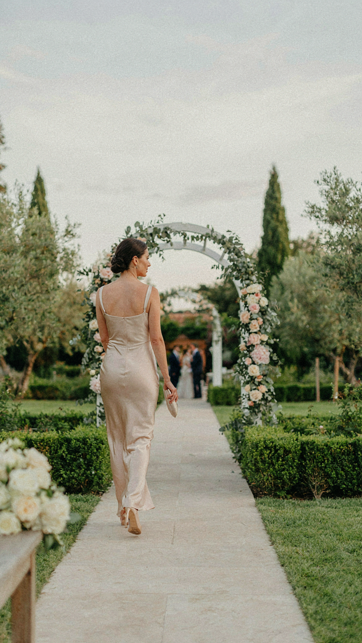 A person confidently walks towards a wedding venue, dressed in comfortable cocktail attire.