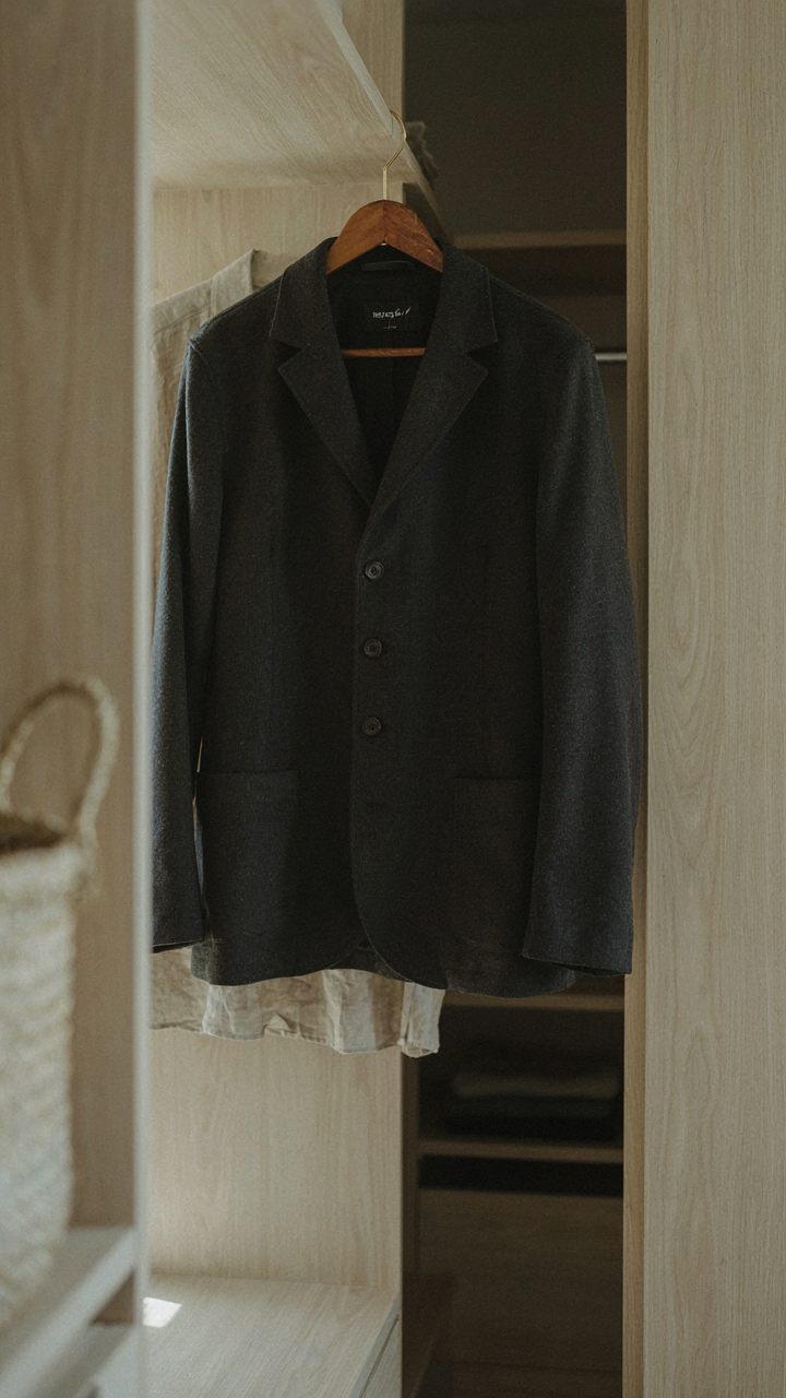 A perfectly tailored dark jacket hangs in an elegant, well-lit closet.