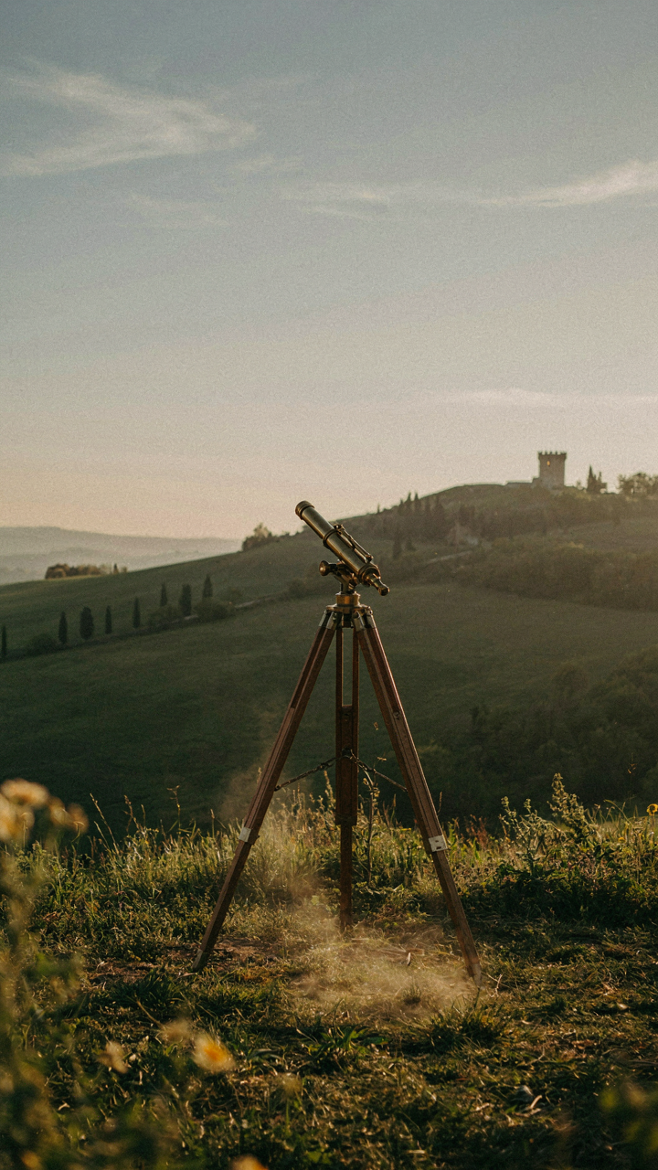 A vintage telescope points towards a distant, illuminated landmark.