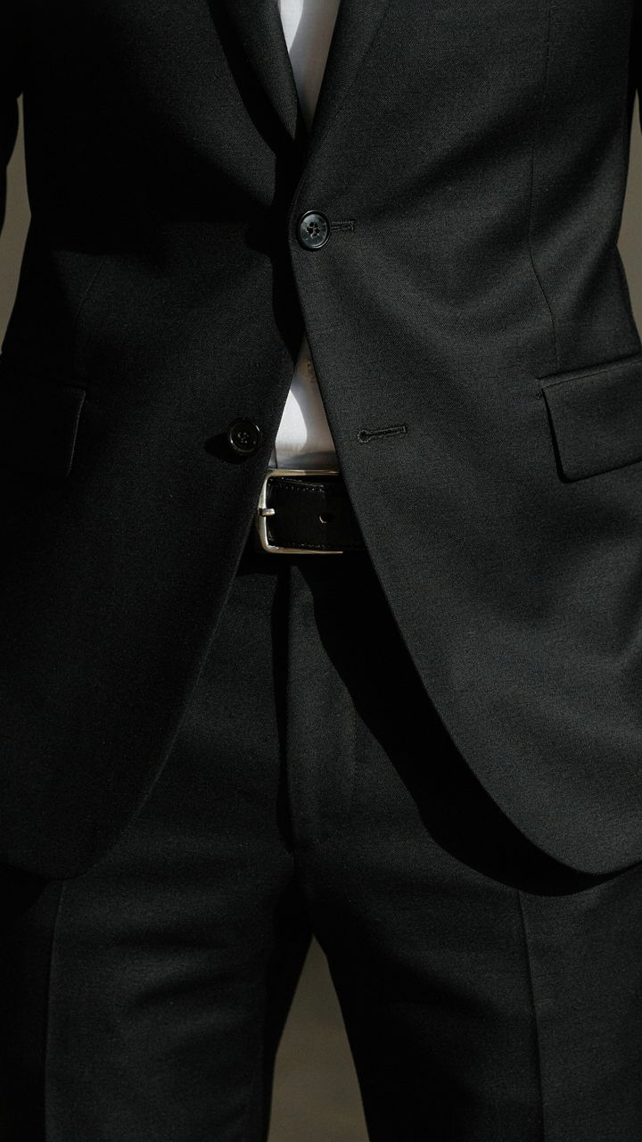 A man's black leather belt completes a sharp, tailored black suit.