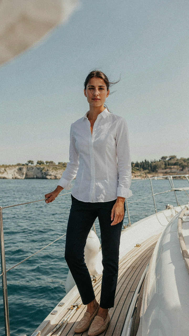 Woman in a simple white linen shirt stands confidently on a yacht.