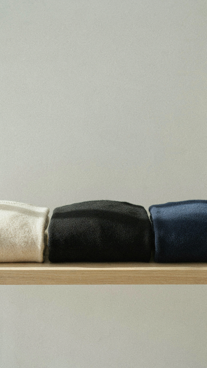 Cream, black, and navy sweaters are folded neatly on a shelf.