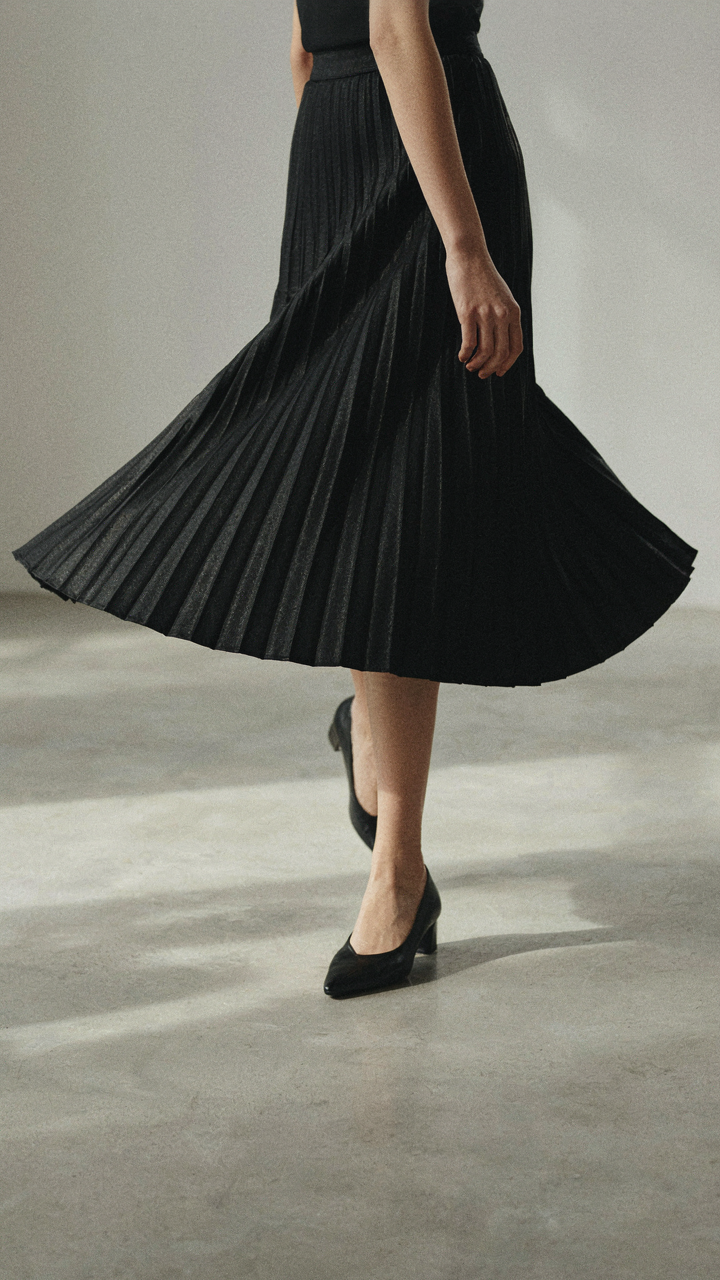 Lower half of a woman in a black pleated midi dress walking confidently.
