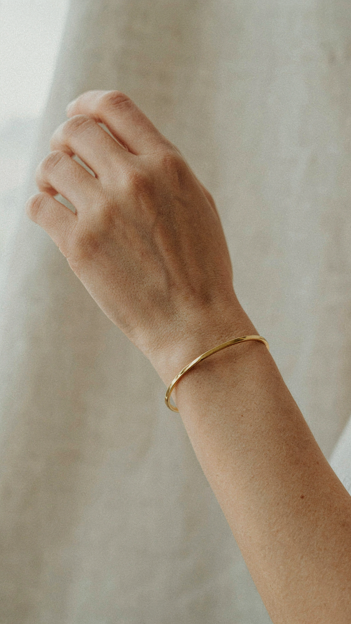 A gold bracelet gleams on a woman's bare wrist.