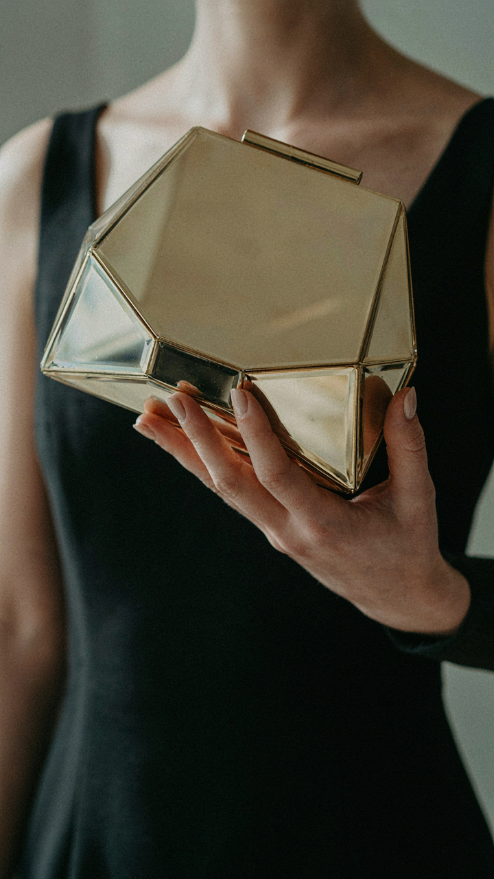 A woman holds a unique, geometric gold metal-frame clutch.