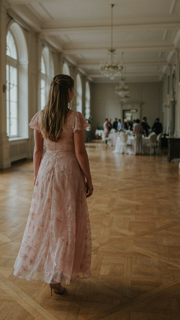 A woman confidently enters a grand hall wearing a romantic style wedding guest dress.
