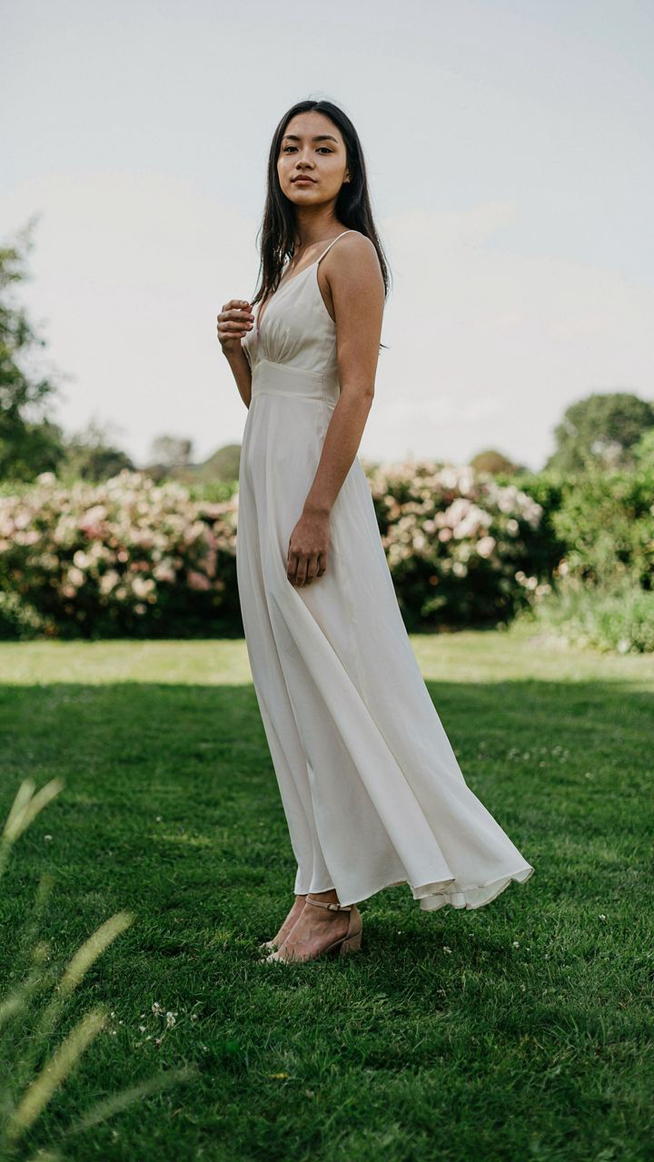 A person stands confidently in a maxi dress and nude wedges on a lawn.