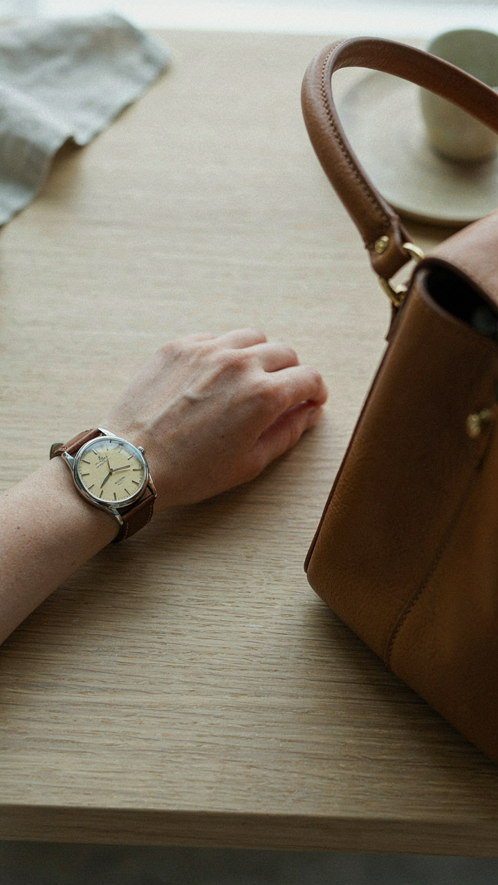 A close-up of a classic metal watch and a structured leather handbag.