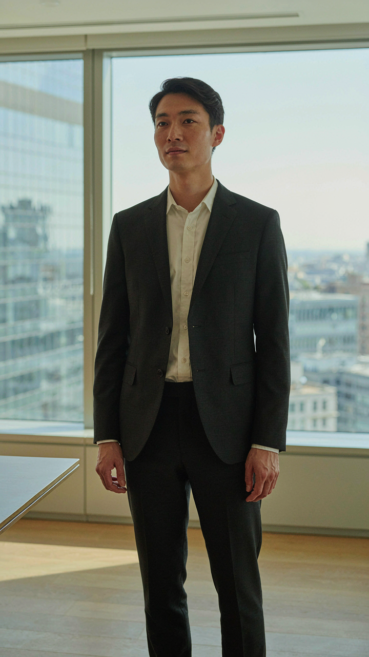 A person in a charcoal blazer and cream shirt, exuding subtle authority.