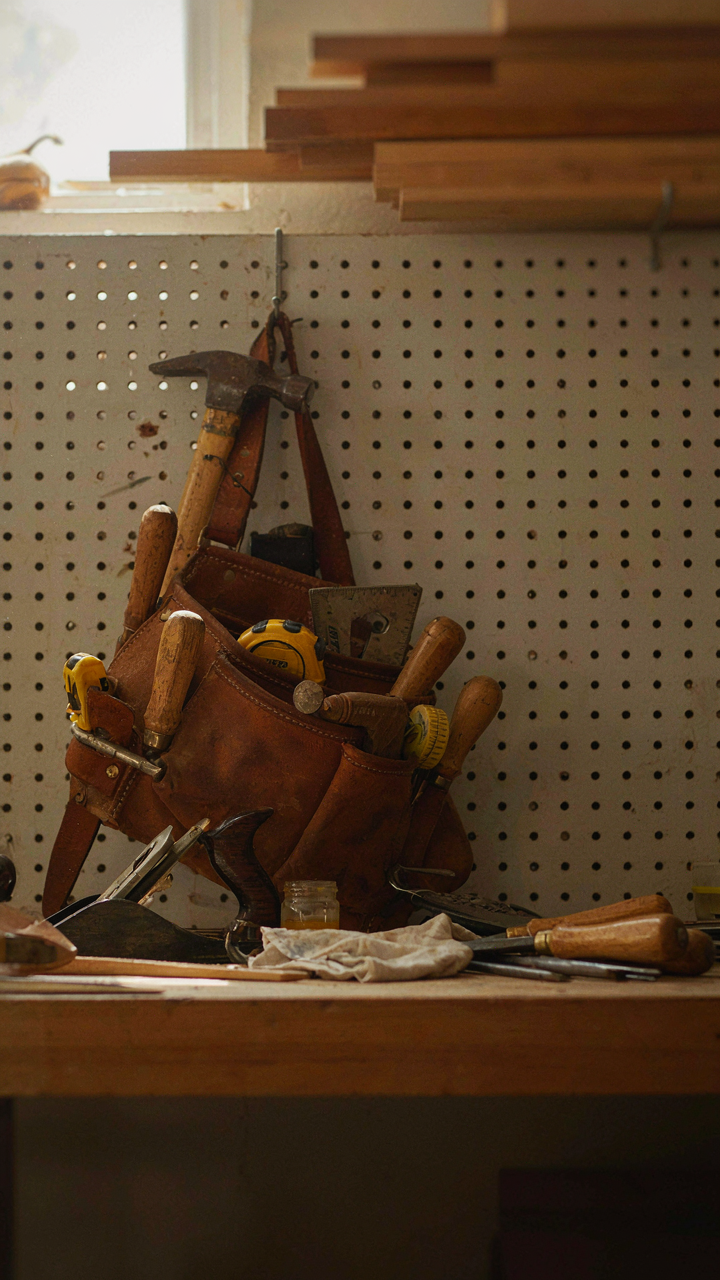 A carpenter's tool belt with tools hangs on a workshop wall.