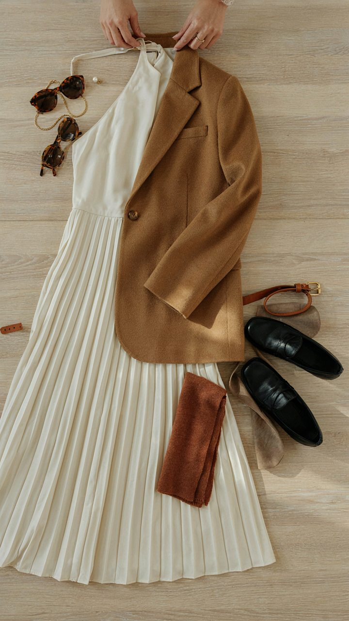 Hands mixing a blazer, shoes, and accessories with a pleated midi dress.