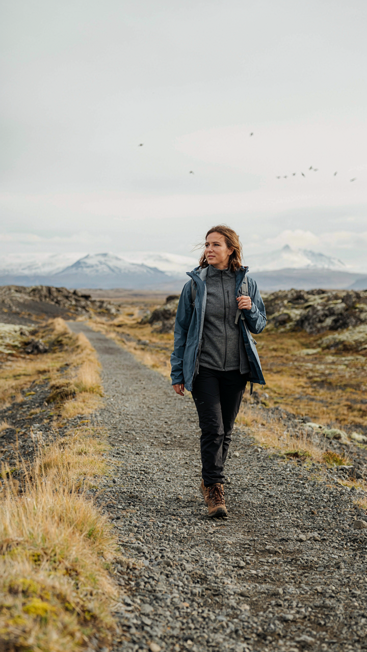 A woman hikes a scenic trail in Iceland wearing a base, mid, and shell layer.