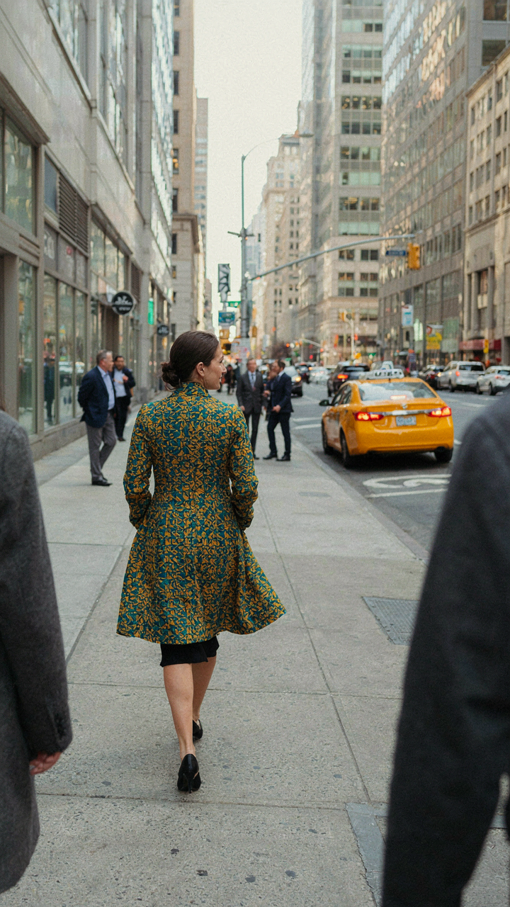 A confident woman in a patterned coat over a black cocktail dress walks away.