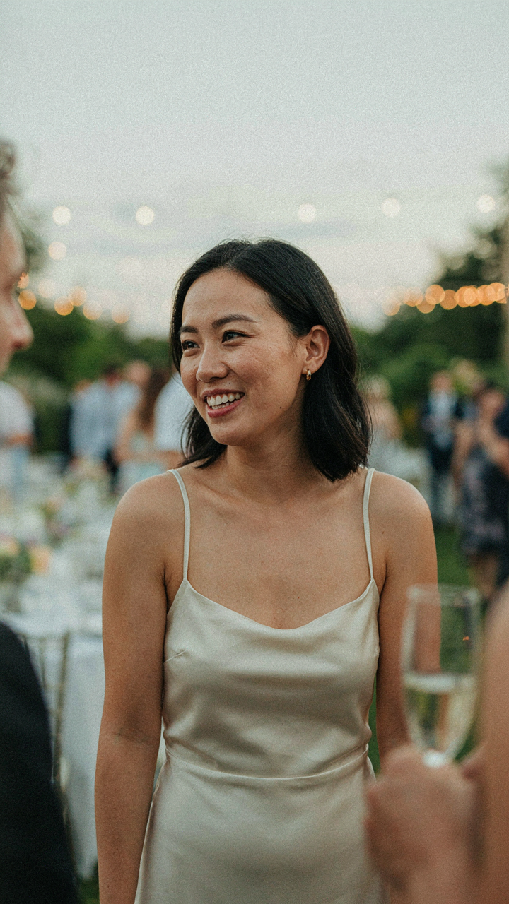 A person smiles confidently at a party, engaged in conversation, wearing a simple outfit.