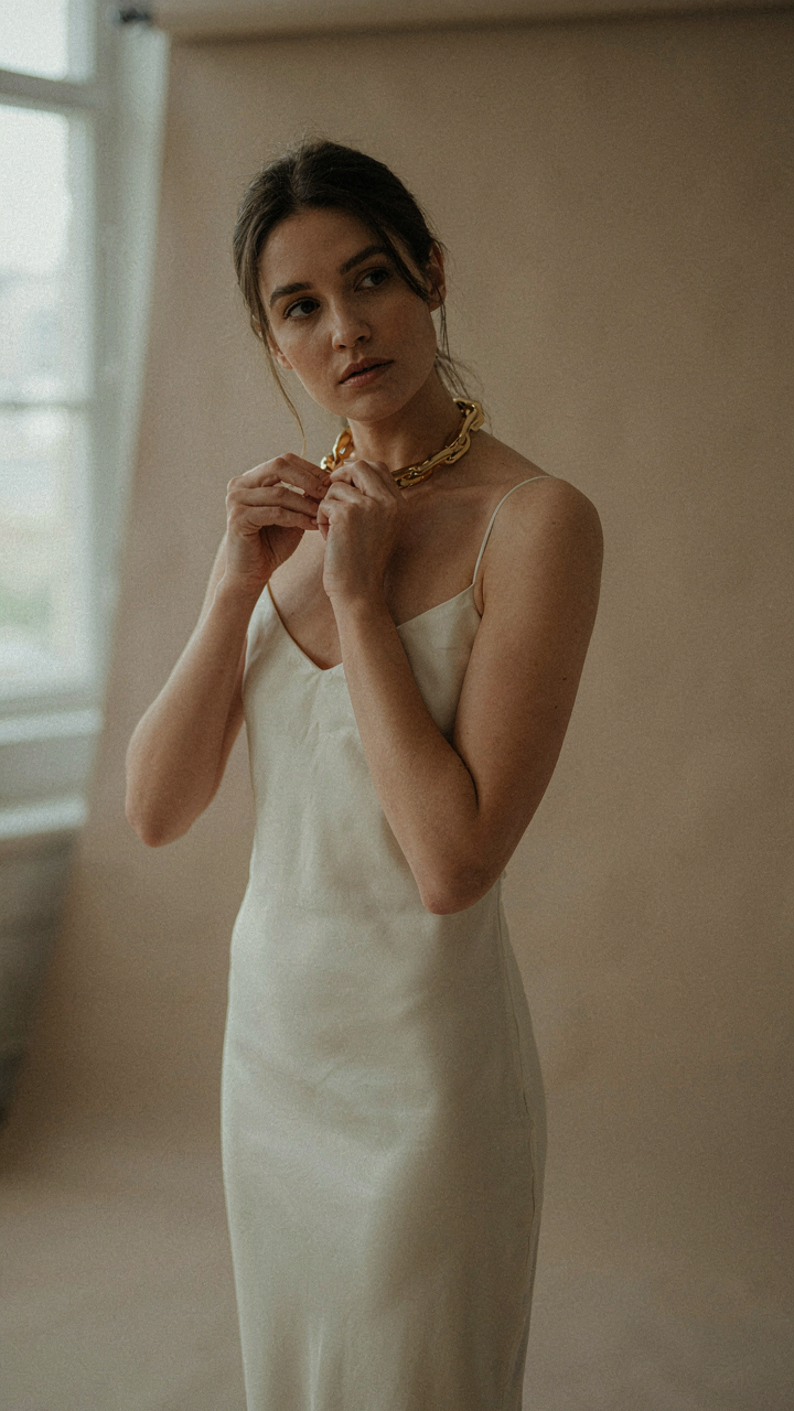 A woman confidently putting on a bold gold necklace.