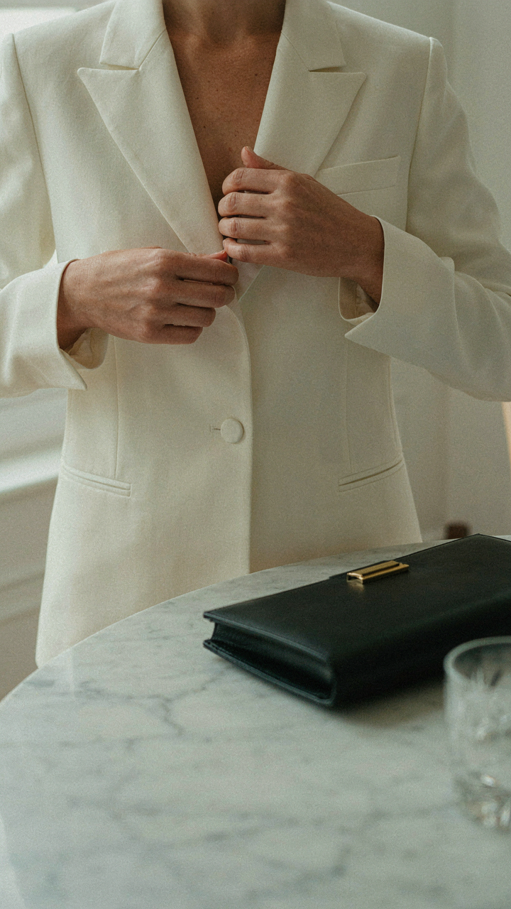 A woman adjusts her tailored silk blazer while a structured clutch waits.