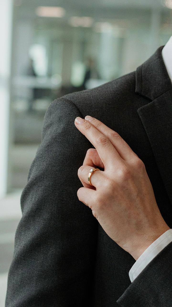 A woman adjusts the shoulder of her dark, well-fitted wool blazer.