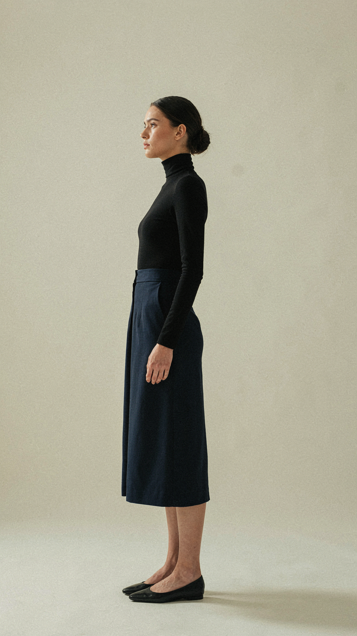 A woman in a black turtleneck and dark sapphire midi dress stands confidently.