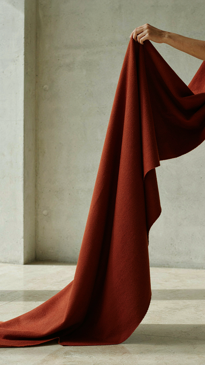 Hand holding a heavy fabric swatch, showing its drape and structure.
