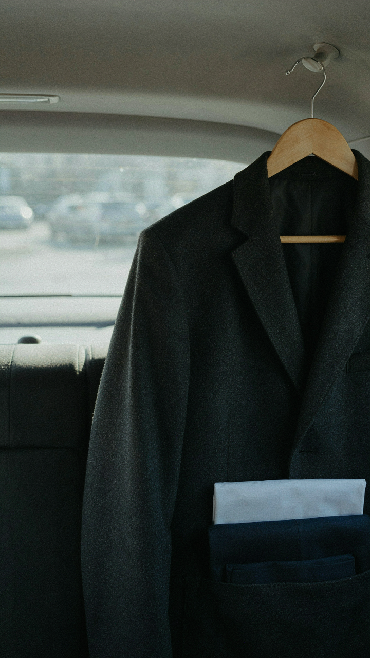 A dark blazer hangs neatly on a hanger inside a car, ready for use.